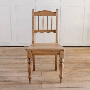 May include: A wooden chair with a slatted back and turned legs. The chair is made of light brown wood and has a simple, classic design.