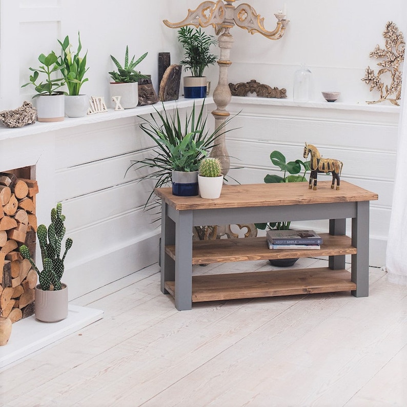 May include: A gray wooden shelf unit with two shelves. The shelf unit is made of reclaimed wood and has a rustic look. The shelf unit is sitting on a white floor in a room with plants and other decor.