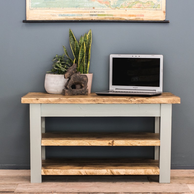 May include: A light blue wooden shelf unit with two shelves. The shelf unit has a rustic wood top and is sitting on a wood floor. A laptop computer, a potted plant, and a wooden figurine are on top of the shelf unit.