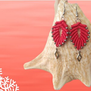 Pode incluir: Brincos vermelhos e prateados com um design em forma de folha. Os brincos s&atilde;o feitos com uma t&eacute;cnica de macram&eacute; e t&ecirc;m um charme em forma de diamante na parte inferior.