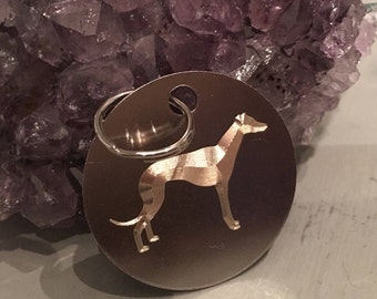 May include: A circular silver-toned metal pet tag featuring a laser-engraved silhouette of a greyhound dog in profile. The tag includes a small circular hole at the top with a silver-toned metal split ring attached for easy collar attachment.
