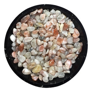 Pode incluir: Uma tigela cheia de pequenos cristais de pedra do sol, laranja, rosa e transparentes, rolados.