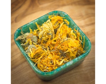 May include: A teal-colored square bowl filled with dried yellow calendula petals. The petals are loose and have a slightly brown hue.