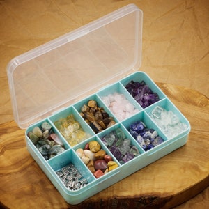 May include: A light blue plastic storage box with a clear lid, divided into nine compartments. Each compartment contains a different type of gemstone, including amethyst, rose quartz, clear quartz, tiger's eye, fluorite, lapis lazuli, and more.