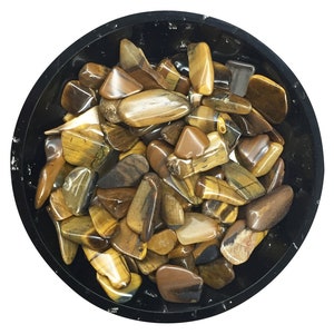 Pode incluir: Uma tigela cheia de pedras de olho de tigre polidas. As pedras são uma mistura de marrom, dourado e preto.