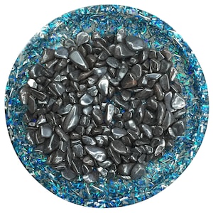 Pode incluir: Uma bandeja redonda de resina transparente com uma borda de glitter azul cheia de pedras de hematita pretas.