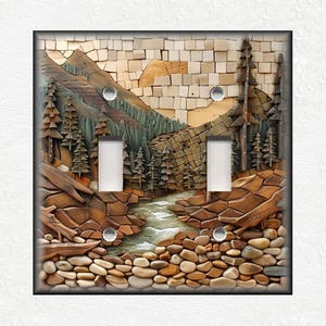 May include: A decorative double light switch cover featuring a mosaic design of a mountain landscape. The artwork includes a river, trees, and a rocky foreground, with a color palette of browns, greens, and beige. The cover is rectangular with a black border.