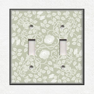 May include: A light green double light switch cover with a white floral pattern.
