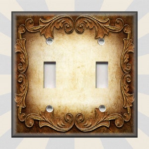 May include: A double light switch cover with a decorative, ornate, gold-colored frame on a brown background.