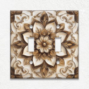 May include: A decorative double light switch cover with a floral design. The cover features a raised, three-dimensional pattern in shades of cream and brown. The design includes a central flower and surrounding floral scrollwork.