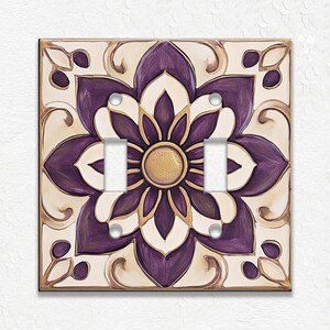 May include: A decorative double light switch cover featuring a floral design. The design has a purple flower with gold accents on a cream background. The cover is square and has a decorative border.