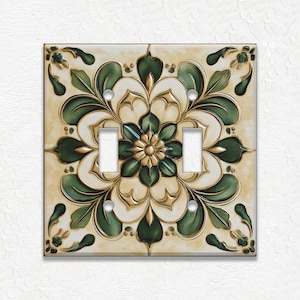 May include: Decorative double light switch cover with a floral design. The cover features a cream-colored background with a detailed pattern of green leaves and gold accents. The design includes a central flower and symmetrical leaf arrangements.