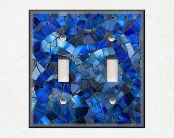Puede incluir: Cubierta de interruptor de luz doble decorativa con un diseño de mosaico en tonos azules. El patrón de mosaico está formado por formas irregulares, creando una apariencia texturizada. Tiene dos aberturas para interruptores basculantes y un borde oscuro.