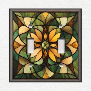 May include: A double light switch cover with a stained glass design featuring a geometric pattern of green, brown, and yellow colors.