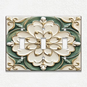 May include: A decorative triple light switch cover with a floral design. The cover features a white, green, and gold color scheme with a raised, textured pattern. The design includes a large central flower and ornate detailing.