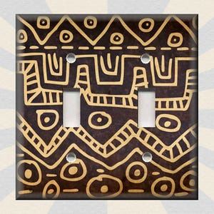May include: A light switch cover with a brown background and a gold geometric pattern. The pattern includes circles, triangles, and zigzags.
