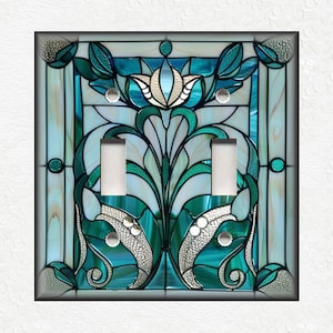 May include: A decorative double light switch cover with a stained glass design. The cover features a teal, turquoise, and white floral pattern with silver accents. The design is framed by a black border.