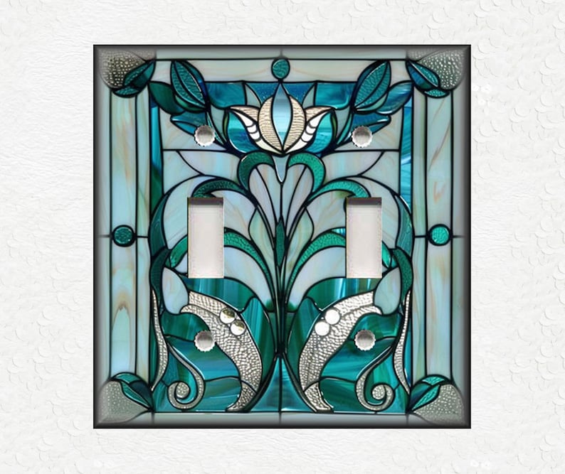 May include: A decorative double light switch cover with a stained glass design. The cover features a teal, turquoise, and white floral pattern with silver accents. The design is framed by a black border.