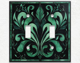 May include: A decorative double light switch cover with a black background and a green floral design. The design features stylized leaves and swirls, with a dark green border. The switch cover has two switch openings and two small, round screw holes.