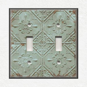 May include: A light blue and white light switch cover with a distressed tin ceiling tile pattern.