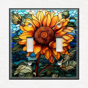 May include: A decorative double light switch cover featuring a stained-glass style sunflower design. The sunflower has yellow and orange petals, a brown center, and green leaves. The background is blue.