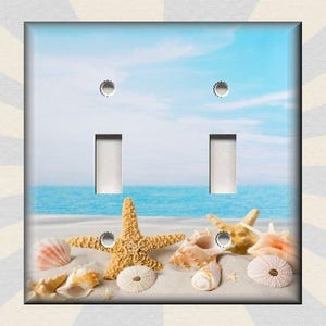 May include: A light switch plate with a beach scene featuring seashells and starfish. The switch plate is white with two toggle switches.