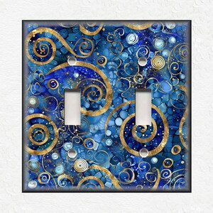May include: A decorative double light switch cover with a blue and gold abstract design. The cover features a swirling pattern with gold accents and two white toggle switches. The design has a dark border.