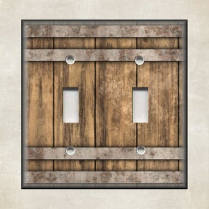 May include: A double light switch cover with a rustic wood and metal design. The cover features a weathered wood plank background with two metal bands and rivets.
