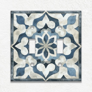 May include: A square light switch cover with a blue, white, and gray floral design. The cover features two switch openings and a decorative pattern reminiscent of a tile. The design includes a central flower and symmetrical shapes.