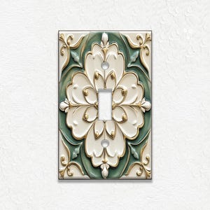 May include: Decorative light switch cover with a floral design. The cover features a white, green, and gold color scheme. The design includes a central toggle switch and ornate floral patterns. The cover is rectangular and has a glossy finish.