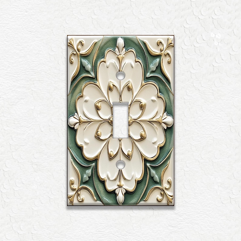 May include: Decorative light switch cover with a floral design. The cover features a white, green, and gold color scheme. The design includes a central toggle switch and ornate floral patterns. The cover is rectangular and has a glossy finish.
