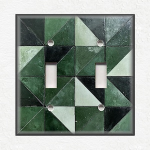 May include: A light switch cover with a geometric pattern of green and white triangles. The switch cover has two toggle switches.