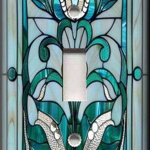 May include: A decorative light switch cover with a stained glass design. The design features teal, white, and silver floral and geometric patterns. The cover has a single switch opening and a rectangular shape. The overall style is reminiscent of Art Nouveau.