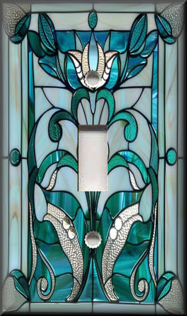May include: A decorative light switch cover with a stained glass design. The design features teal, white, and silver floral and geometric patterns. The cover has a single switch opening and a rectangular shape. The overall style is reminiscent of Art Nouveau.