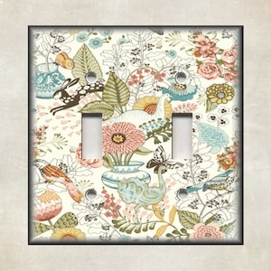 May include: A light switch cover with a floral pattern featuring birds, butterflies, and rabbits. The background is white with a light blue, pink, and green floral design.