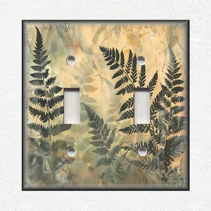 May include: A light switch plate with a fern pattern in shades of green and brown on a beige background.