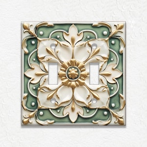 May include: A decorative double light switch cover with a floral design. The cover features a white and gold flower pattern on a green background. The design is ornate and detailed, with a vintage aesthetic.