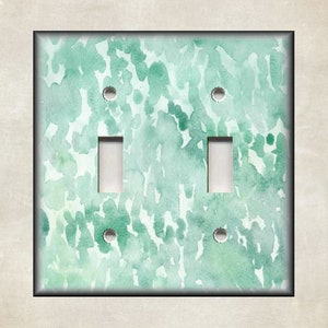 May include: A light green and white watercolor design light switch cover with two toggle switches.