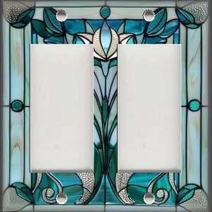 May include: A decorative double light switch cover with a stained glass design. The cover features a teal, green, and white floral pattern with a silver border. The two switch openings are white.