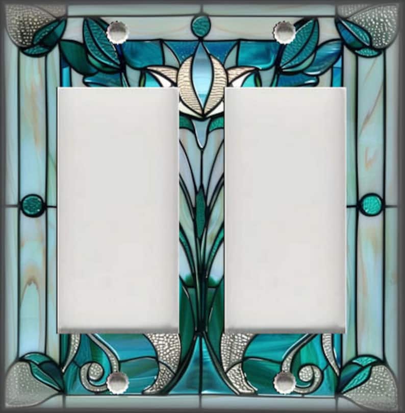 May include: A decorative double light switch cover with a stained glass design. The cover features a teal, green, and white floral pattern with a silver border. The two switch openings are white.
