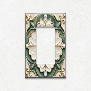 May include: A decorative light switch cover with a floral design. The cover features a rectangular shape with a central opening. The design incorporates white, green, and gold colors, with a raised, textured pattern. The background is white.