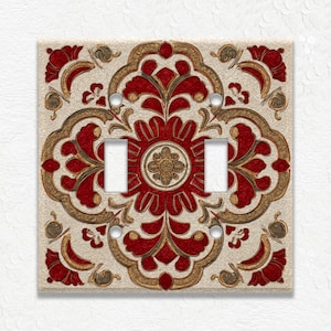May include: Decorative double light switch cover with a floral design. The cover features a cream background with red and gold floral patterns. The design includes a central flower and ornate corner accents.