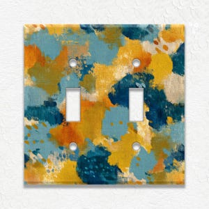 May include: A double light switch cover with an abstract design. The cover features a vibrant mix of colors, including yellow, teal, orange, and white, creating a textured, artistic appearance. The cover has two switch openings and four screw holes.