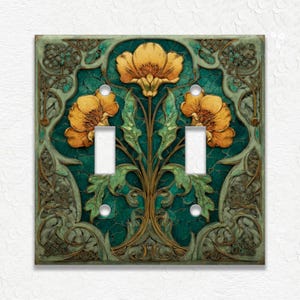 May include: A decorative double light switch cover featuring a floral design. The cover has a teal background with a gold and green floral pattern. Three yellow flowers are centered on the cover, with two toggle switch openings.
