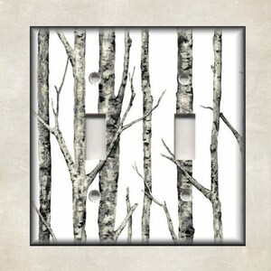May include: A decorative double light switch cover featuring a black and white birch tree design. The cover has a neutral beige border and a black frame, creating a natural, rustic aesthetic. The design includes two switch openings.