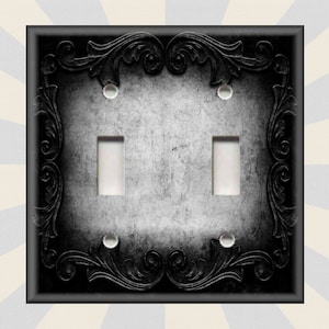 May include: Black and white light switch cover with a decorative ornate border. The switch cover has a distressed, aged look.