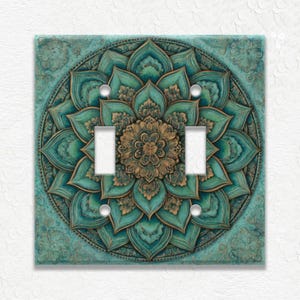 May include: A decorative double light switch cover featuring a teal and gold mandala design. The floral pattern is embossed with intricate details. The cover has two toggle switch openings and is mounted on a white wall.