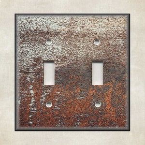 May include: A double light switch cover with a rustic, weathered, and rusty metal design. The cover has a light brown and gray color with hints of orange and red.