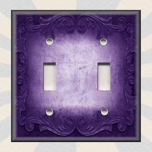 May include: Purple light switch cover with an ornate, floral design. The switch cover has two toggle switches.