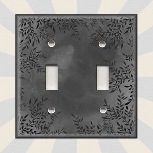 May include: A black light switch cover with a white switch and a floral design. The design features black leaves and branches on a gray background.
